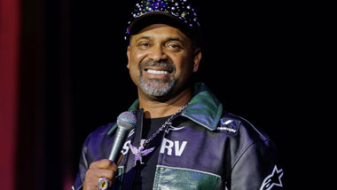 Mike Epps holding a microphone and smiling toward the camera.